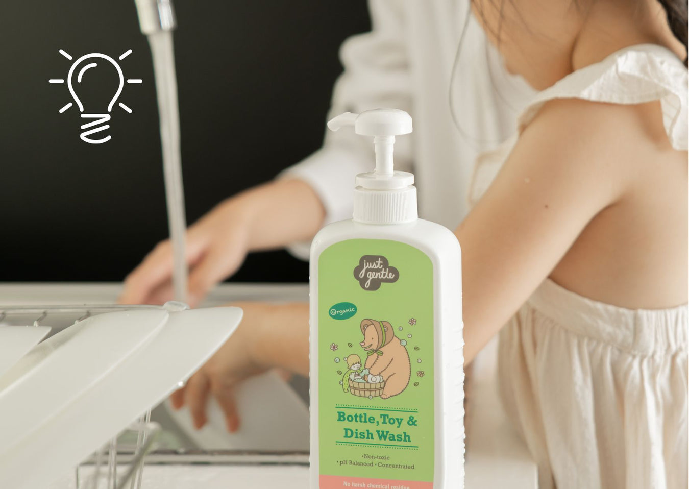 Just Gentle Bottle, Toy & Dish Wash pump bottle at a kitchen sink while parent helps toddler rinse dishes. Just Gentle