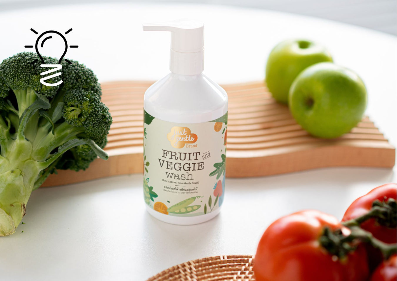Just Gentle Fruit & Veggie Wash pump bottle on a kitchen counter, framed by fresh broccoli, green apples and tomatoes.