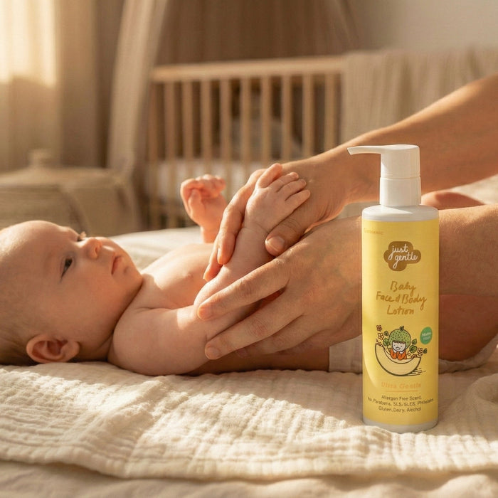 Baby lying on a bed with a bottle of Just Gentle baby lotion next to it, in a warm and cozy room.