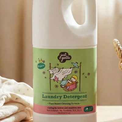 Just Gentle Plant-Based Laundry Detergent beside a basket of folded baby clothes