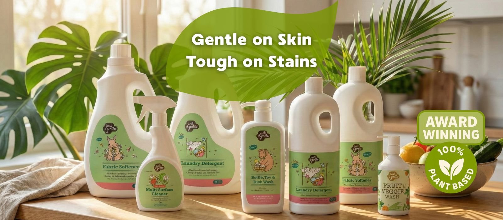Collection of 'Just Gentle' cleaning products on a wooden surface with plants in the background