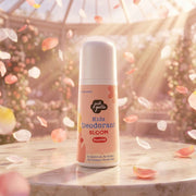 A dreamy, beautifully lit product shot of the Just Gentle 'Bloom' deodorant resting on a marble surface inside a sunlit greenhouse. Soft pink and white flower petals are floating in the air around the bottle.