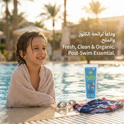 Child by a pool with a bottle of Just Gentle swim and sport product, surrounded by palm trees.