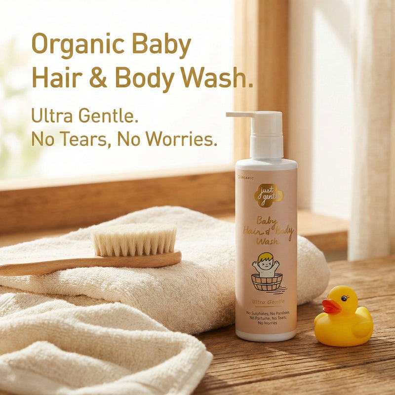 JUST GENTLE Organic baby hair and body wash bottle with a brush, towel, and rubber duck on a wooden surface.