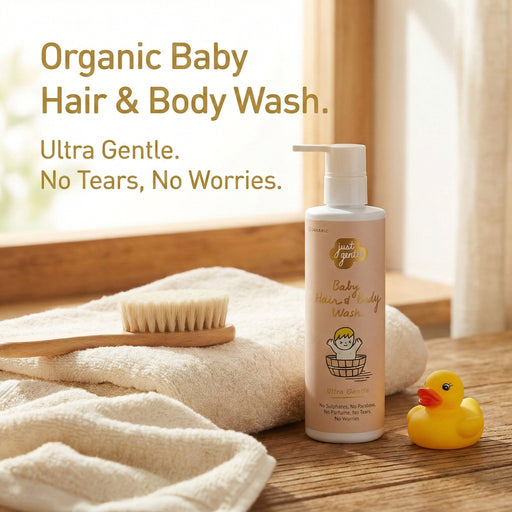 JUST GENTLE Organic baby hair and body wash bottle with a brush, towel, and rubber duck on a wooden surface.