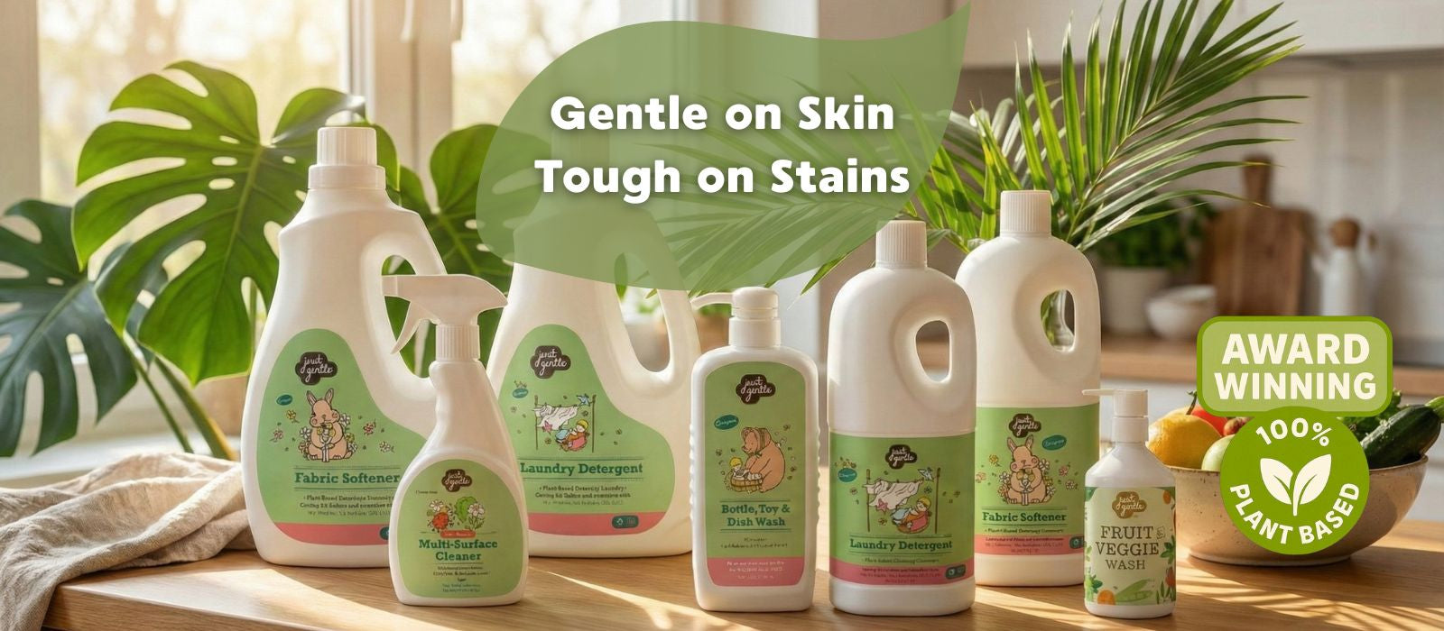 Collection of 'Just Gentle' cleaning products on a wooden surface with plants in the background