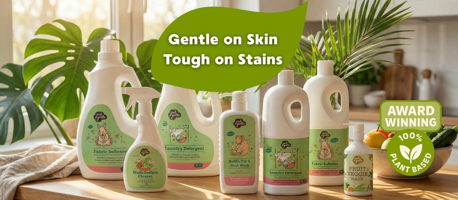 Collection of 'Just Gentle' cleaning products on a wooden surface with plants in the background