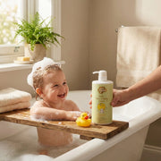 Child in a bathtub with a wooden step, holding a bottle of Just Gentle Kids Wash, with a rubber duck and towels in the background.