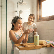 Woman and child in a bathroom with a bottle of 'Just Gentle' Kids shampoo on a tray.