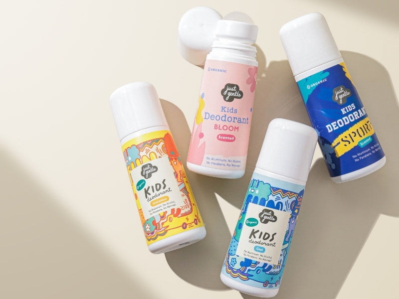 Four bottles of 'Just Gentle' Kids' deodorant on a beige background
