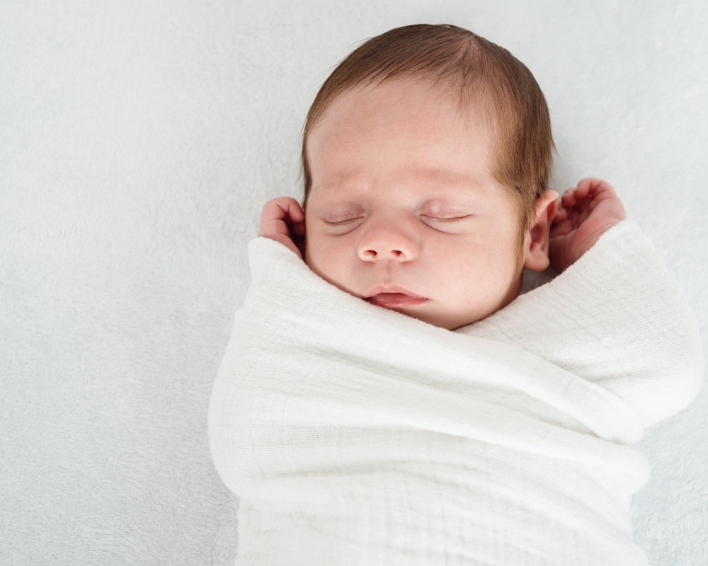 Newborn baby wrapped in a white blanket on a light gray background. Nust Gentle Pure Start Ages 0-2 Banner.