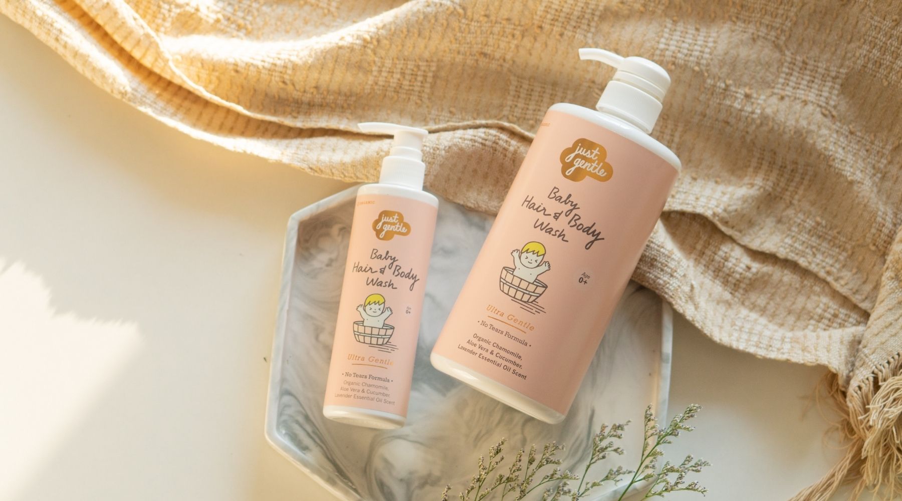 Two bottles of 'Just Gentle' Baby Hair & Body Wash on a textured fabric background