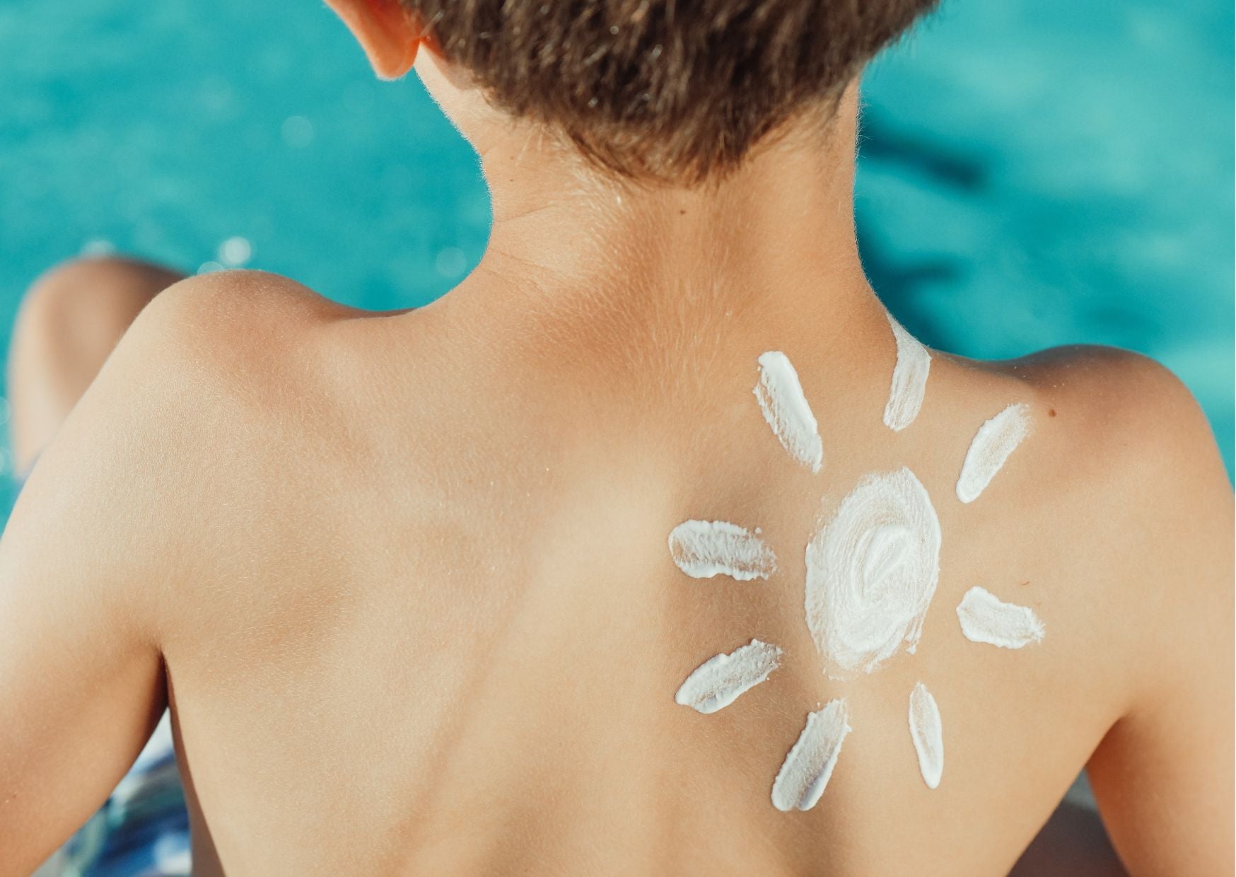 Child sitting poolside with a sun-shaped pattern of white sunscreen spread across upper back and shoulder blades | Just Gentle