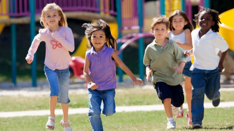 Children running on a grassy area with colorful playground equipment in the background
