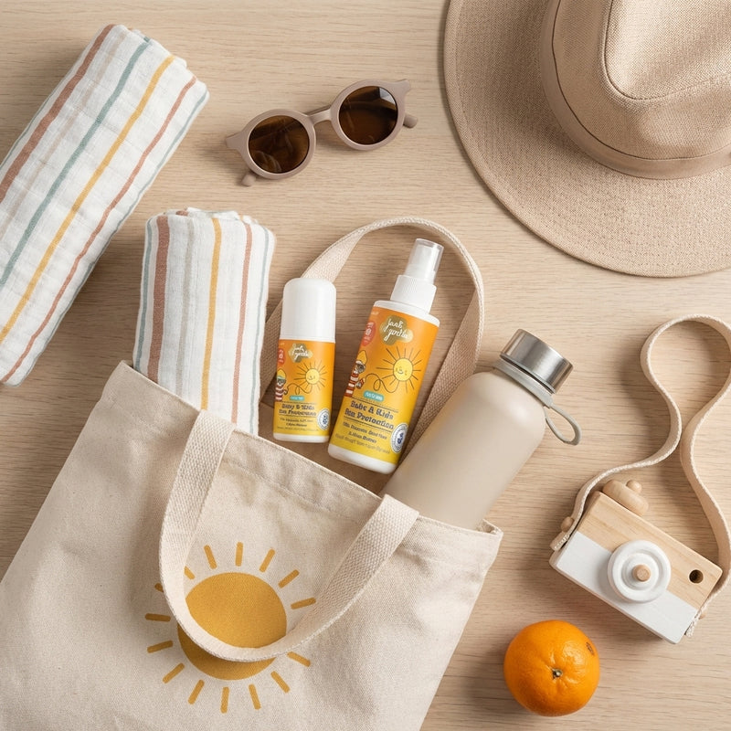 Just Gentle Sunscreen bottles, sunglasses, hat, water bottle, and camera on a wooden surface with a tote bag featuring a sun design.