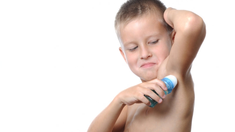Child applying deodorant to armpit on a white background