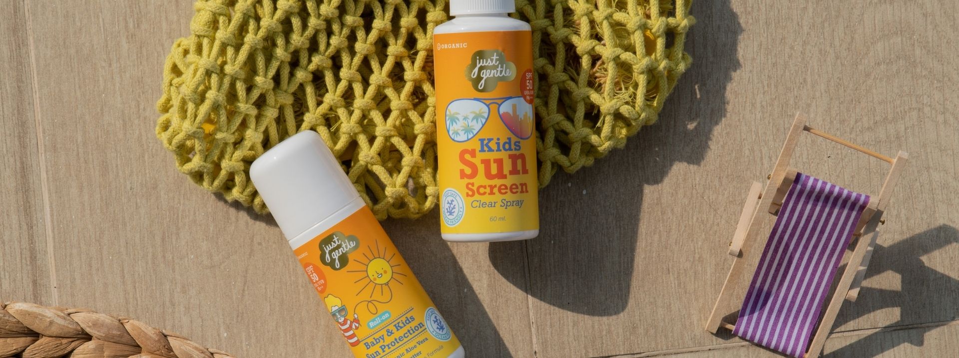 Two bottles of Baby and Kids' Sunscreen with a yellow mesh bag on a wooden surface. Just Gentle