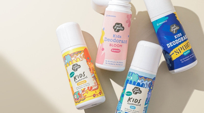 Four 'Just Gentle' organic Kids deodorant bottles with colorful labels on a beige background