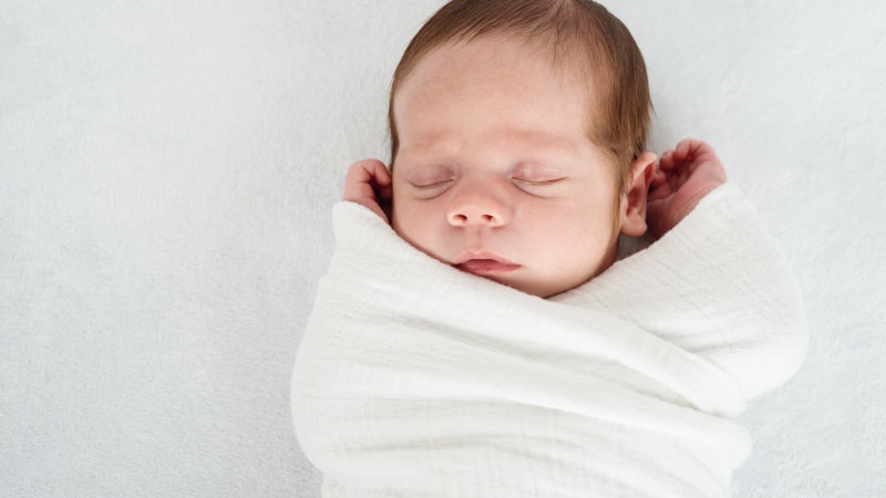 Newborn baby wrapped in a white blanket on a light gray background